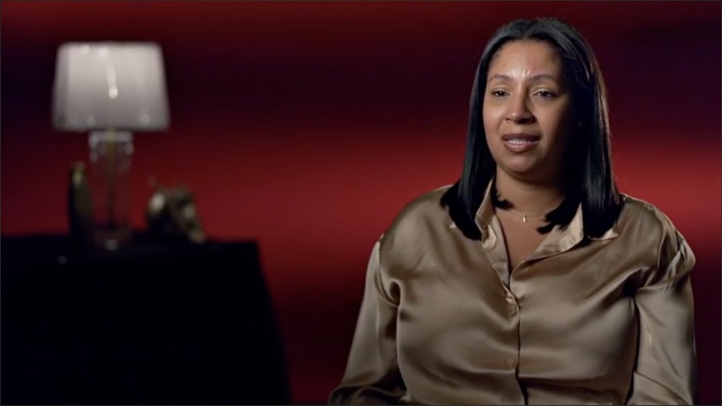 Interview subject lit against a deep red gradient backdrop with a soft-focus practical lamp