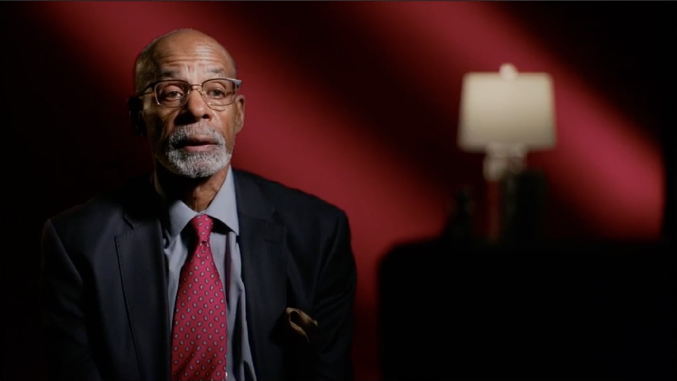 Interview subject lit against a deep red gradient backdrop with a soft-focus practical lamp