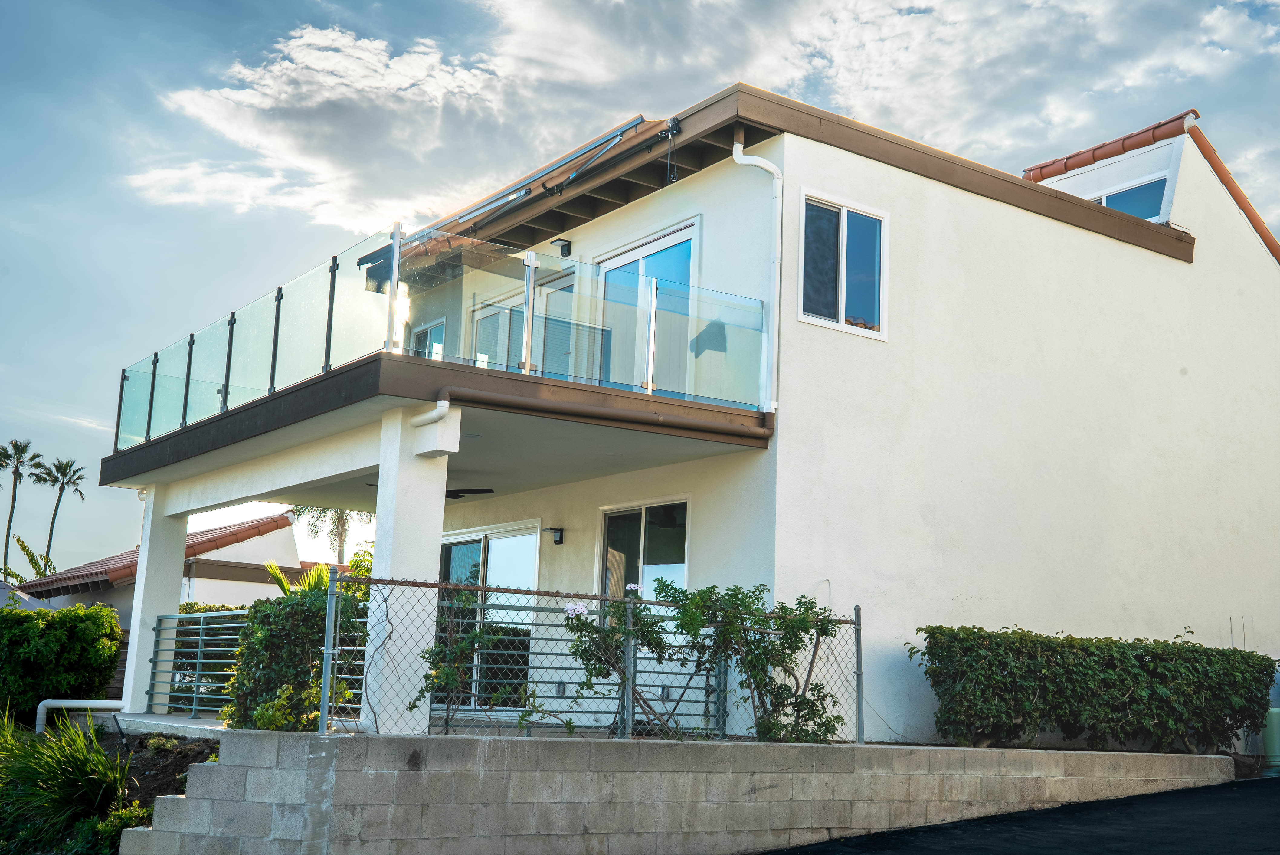 Two-story home exterior with glass-railed balcony and palm trees